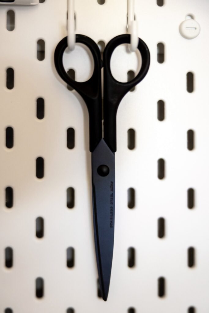 Black hair-cutting shears hanging on a white pegboard